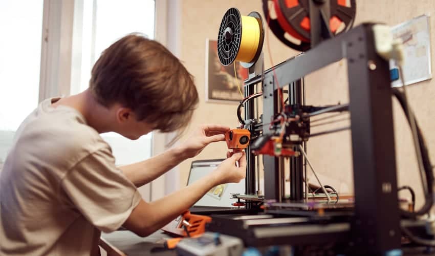 A close-up of hands performing maintenance on a 3D printer’s nozzle