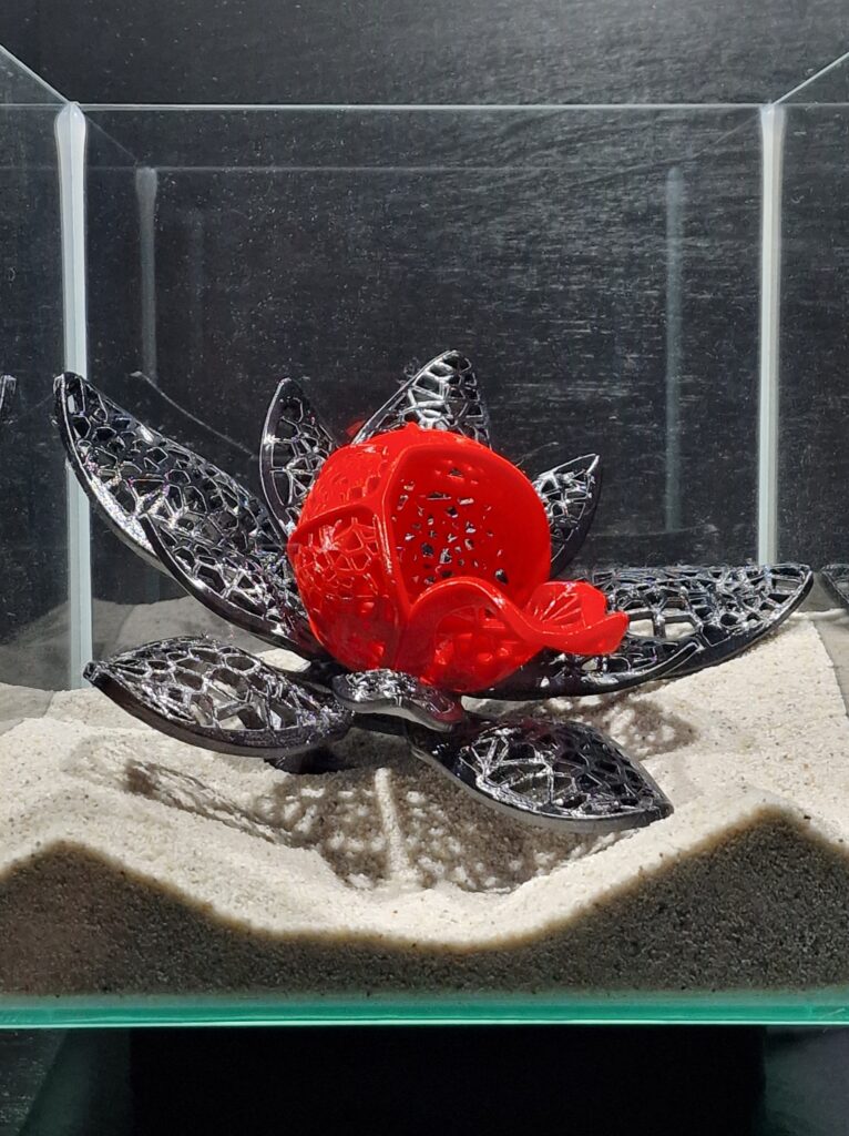 Detailed close-up of the elegant betta fish cave by Aquireef3D, showcasing its intricate lotus flower design with a striking red center and decorative black petals, placed on a sandy aquarium substrate.