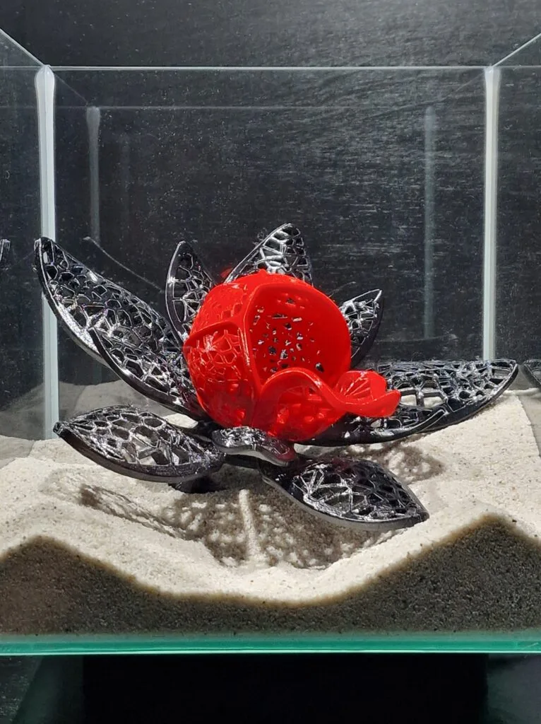 Detailed close-up of the elegant betta fish cave by Aquireef3D, showcasing its intricate lotus flower design with a striking red center and decorative black petals, placed on a sandy aquarium substrate.