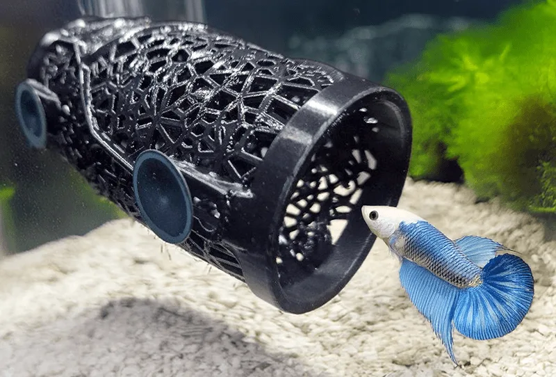 Betta fish cylindrical 3d print cave with a small betta fish checking it's inner part. Voronoi design helps save the filament and provides a perfect suit for bettas. A design by Aquireef3D.
